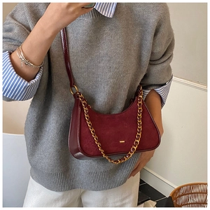 Detalle de bolso bandolera de ante burdeos con cadena dorada sobre jersey de punto