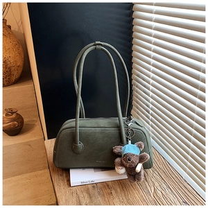 Détail du sac Boston en daim vert foncé avec texture vintage et breloque petit ours