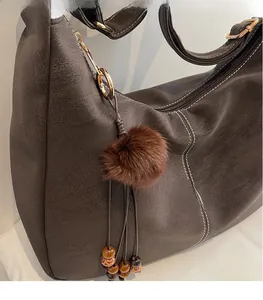 Detail of dark brown faux fur pompom charm with vintage wooden beads on leather bag