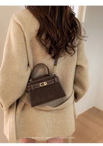 Detail of dark brown suede trapezoid bag with contrast stitching and metal twist lock