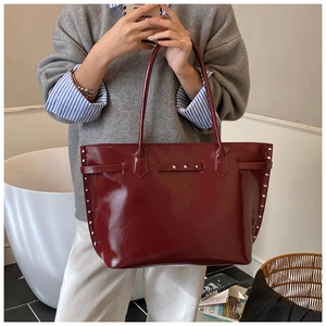 Macro shot of silver studs and glossy burgundy patent leather on a spacious tote bag