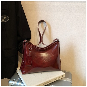 Detail of burgundy leather bucket bag with glossy finish on a textured travel setting