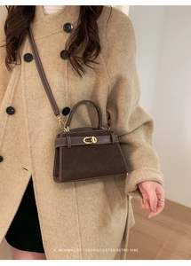 Detail of vintage suede crossbody bag in dark brown with gold twist-lock on beige coat