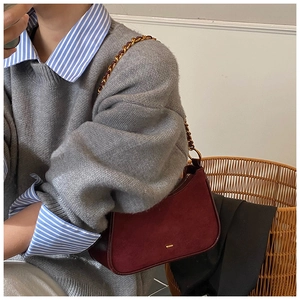 Detalle de bolso medialuna de ante rojo oscuro con cadena dorada y cierre metálico