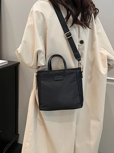Large black nylon tote bag with golden hardware and wide shoulder strap shown on model