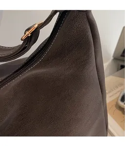 Close-up of brown suede shoulder bag featuring contrast stitching and gold buckle