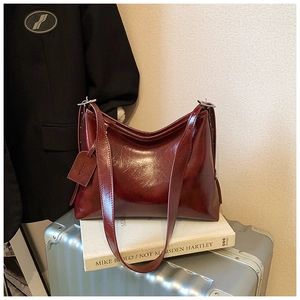Detail of burgundy glossy leather hobo bag with wide shoulder strap on art book