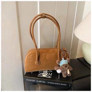 Gros plan sur un sac Boston en daim marron avec pendentif ours sur des livres