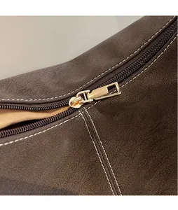 Detail of gold metal zipper and white contrast stitching on dark brown leather bag