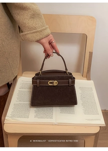 Close-up of retro brown suede handbag with golden buckle on a wooden chair and books