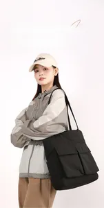 Detail of black large capacity tote bag with dual front pockets on model in windbreaker