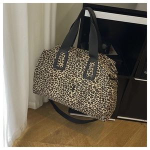 Dettaglio della borsa da viaggio leopardata con tracolla nera su pavimento in legno