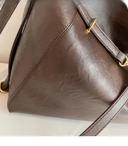 Close-up of soft brown leather bag with dual-stitching and golden metal hardware ring