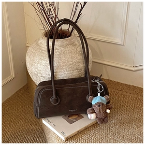 Détail du sac Boston en daim marron foncé avec surpiqûres et pendentif ours