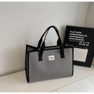 Détail d'un sac cabas à carreaux gris avec poignées noires et étiquette carrée minimaliste