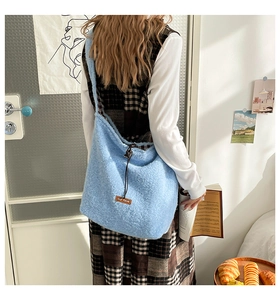 Detail of light blue fuzzy fleece tote bag featuring brown leather logo patch and drawstring