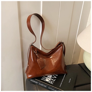 Detail of a brown oil-waxed leather shoulder bag with smooth texture and side tag