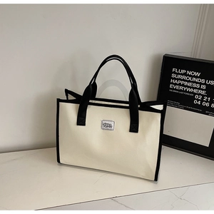 Vue détaillée du sac cabas en toile crème avec poignées noires et écusson logo brodé