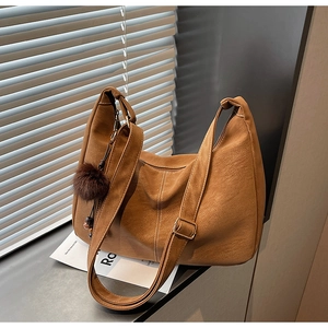 Detail of dark caramel tote bag featuring contrast stitching and plush ball charm decoration