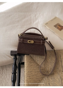 Detail of vintage dark brown handbag with contrast stitching and golden clasp on a woven chair