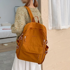 Detail eines ingwergelben Rucksacks aus strapazierfähigem Stoff mit Sticklogo auf der Rückseite