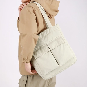 Close-up of cream large capacity tote bag with dual front flap pockets on model