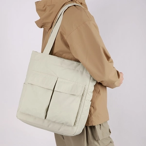 Detail view of beige utility tote bag showing front flap pockets and durable nylon texture