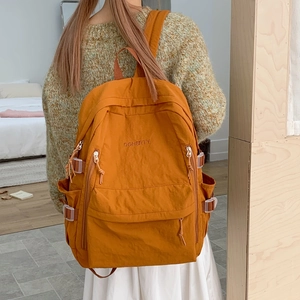Detailaufnahme des ingwergelben Nylon-Rucksacks mit gesticktem Doherty-Schriftzug und Taschen