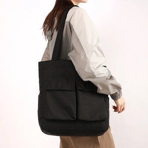 Detail view of a large black shoulder bag featuring two practical front flap pockets