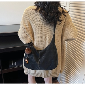Black hobo bag with contrast stitching and fuzzy pendant worn with a warm knit sweater