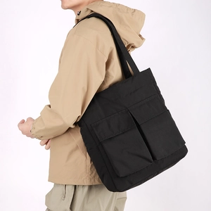 Black utility tote bag with large double pockets and nylon shoulder strap shown on model