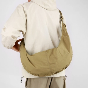 Back view of a khaki nylon crescent crossbody bag worn by a model on white background