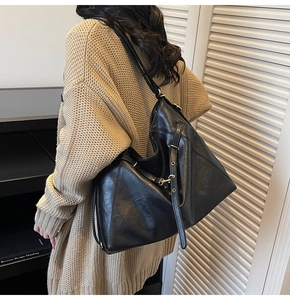 Side view of large black faux leather tote bag with lychee texture on beige sweater