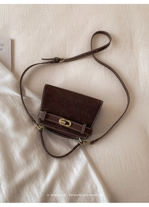 Macro shot of retro dark brown crossbody bag with suede texture and gold oval clasp detail