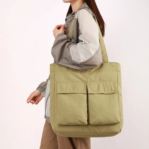 Detail of olive green quilted tote bag with large front flap pockets on model shoulder