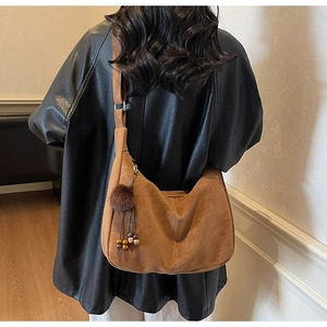Close-up of brown suede hobo bag with plush ball charm and beaded detail on shoulder