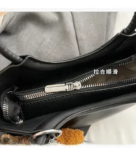 Dettaglio macro della cerniera in metallo argentato su borsa in pelle nera con pompon