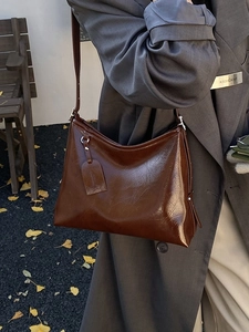Large brown oil wax leather bucket bag worn by model in an autumn street setting