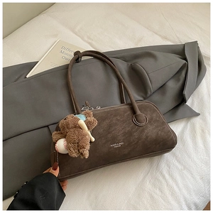 Detailed close-up of dark brown suede shoulder bag with bear pendant and logo