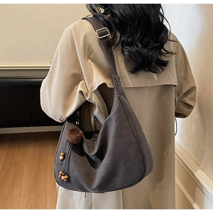 Detail of hobo bag featuring contrast white stitching and decorative plush ball charm