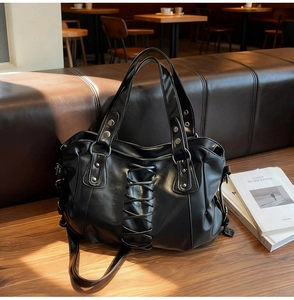 Close-up of a black punk tote bag with rivet straps on a cafe bench background