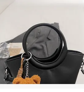 Dettaglio di una borsa a secchiello in pelle nera con ciondolo a forma di orso bruno