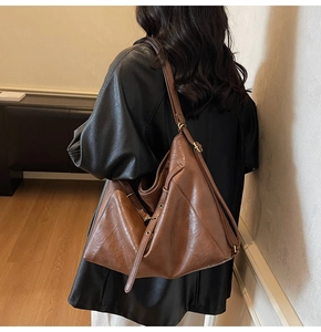 Detail of adjustable metal buckle and textured brown leather shoulder strap on tote bag