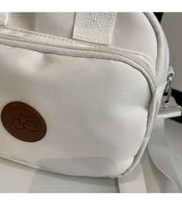 Macro detail of white canvas shoulder bag with zipper and round brown leather patch