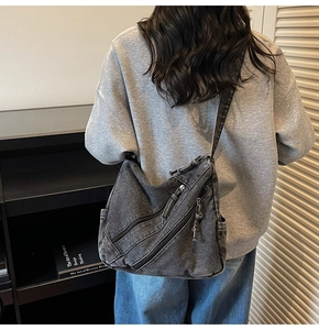 Detail of grey washed denim crossbody bag featuring triple zipper design and wide strap