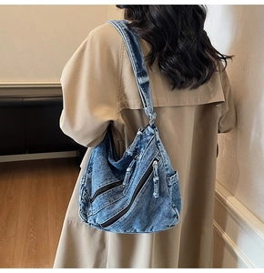 Detail of blue washed denim hobo bag featuring multiple diagonal zippers and large capacity