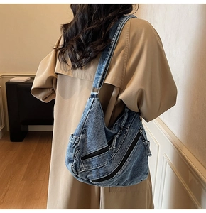Detail of blue denim hobo bag featuring multiple zip pockets and adjustable metal ring