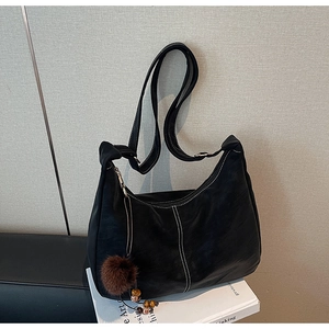 Detail of black matte leather hobo bag featuring contrast white stitching and fur ball charm