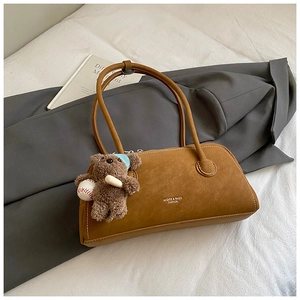 Close-up of caramel matte leather handbag with plush bear charm on grey suit background
