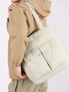 Minimalist beige tote bag with front utility pockets worn by model for daily commute
